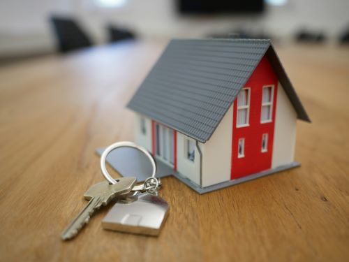 Een sleutelhanger met huissleutels en een miniatuurhuisje op een houten tafel.